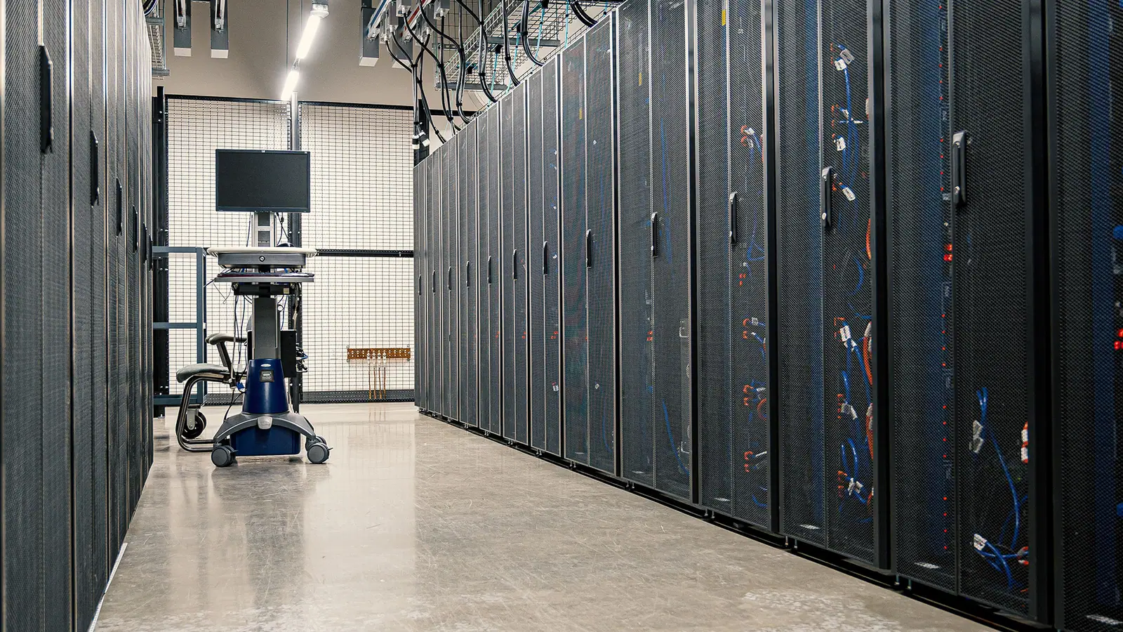 An aisle between rows of network cabinets in a server room, a monitor cart at the far end